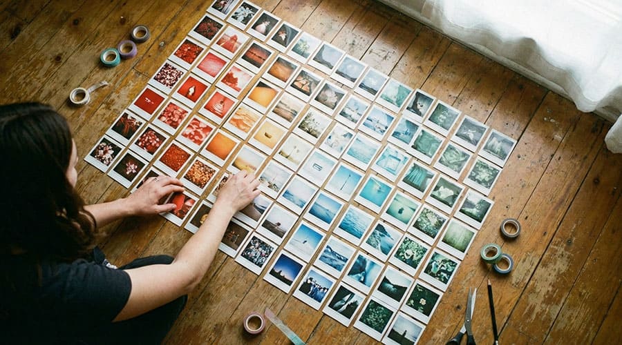 Person arranging mini square photos on the floor into a layout