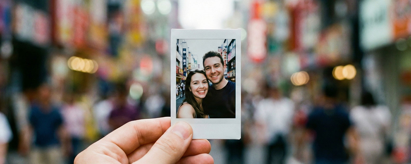 A hand holding a small Instax Mini print against a colorful, blurred background