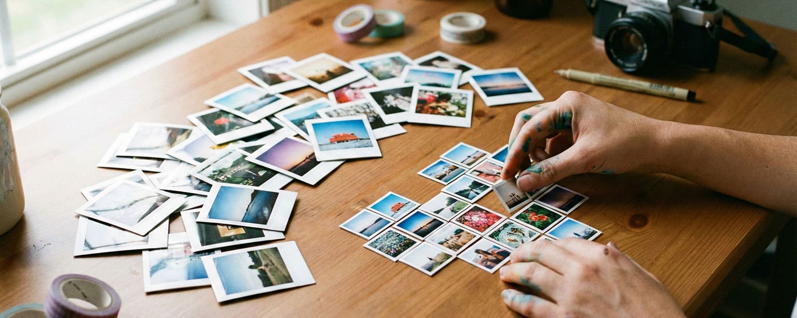 A creative workspace table with a scattered pile of colorful 2x2 mini square photos and some being arranged into a heart shape.